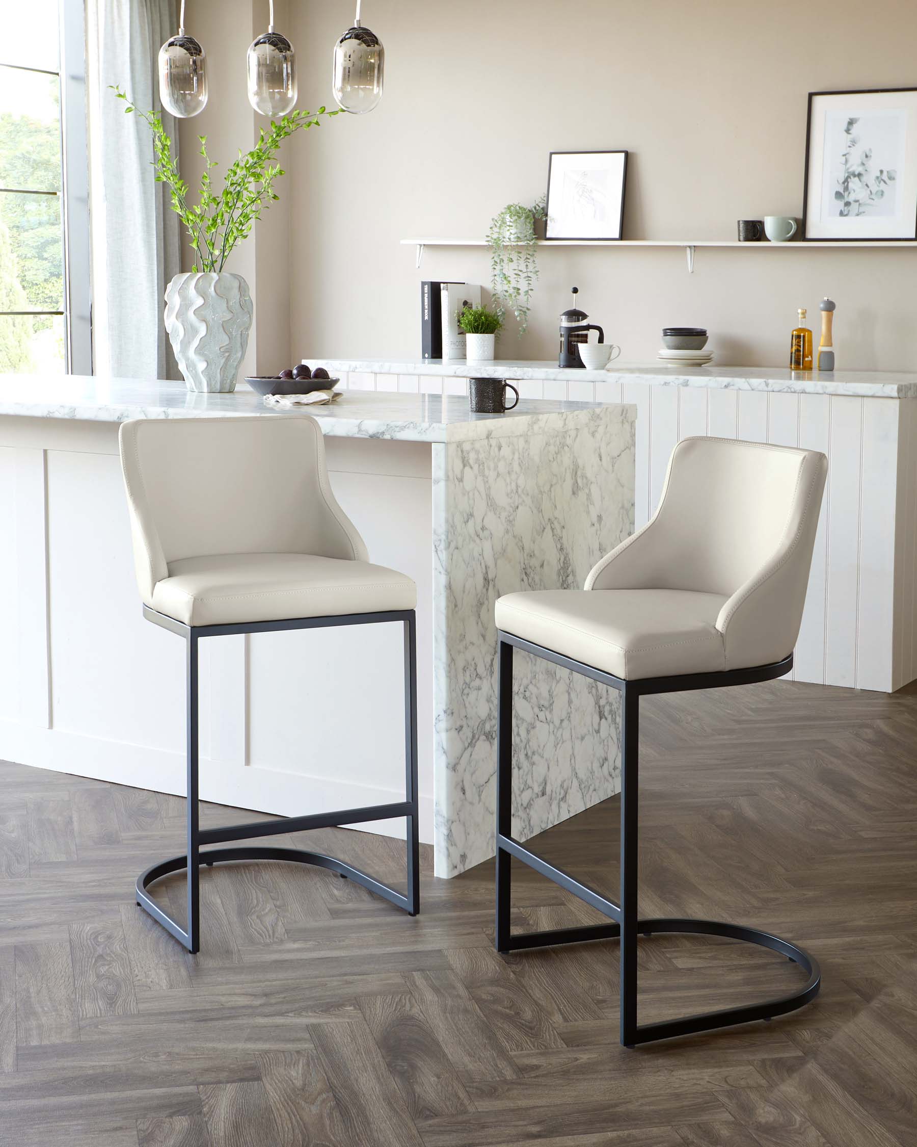 Elegant modern kitchen bar stools with cream-colored faux leather upholstery and sleek black metal legs in a contemporary kitchen setting.