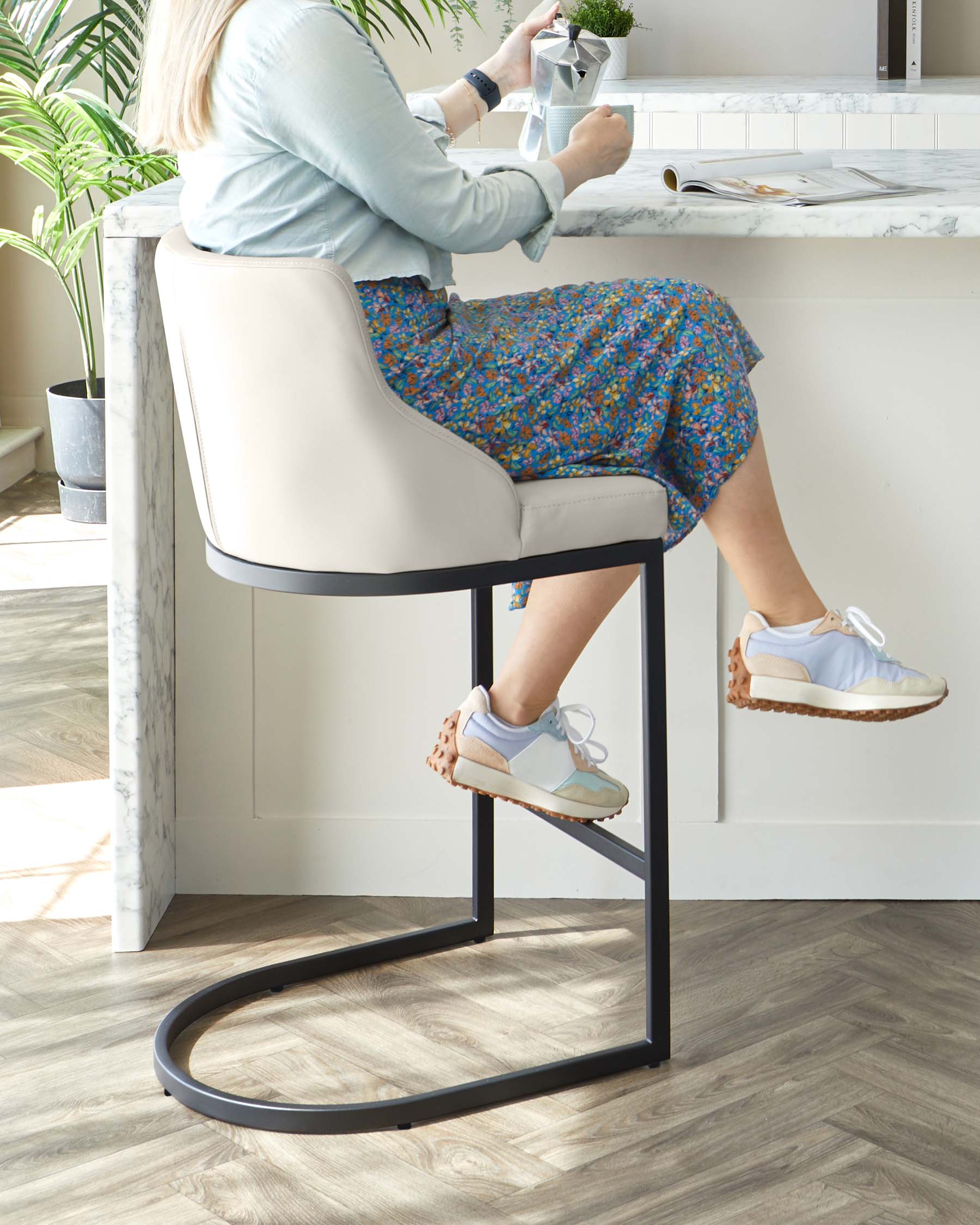 Modern bar stool with sleek black metal frame and a curved, padded backrest and seat in a light beige upholstery.