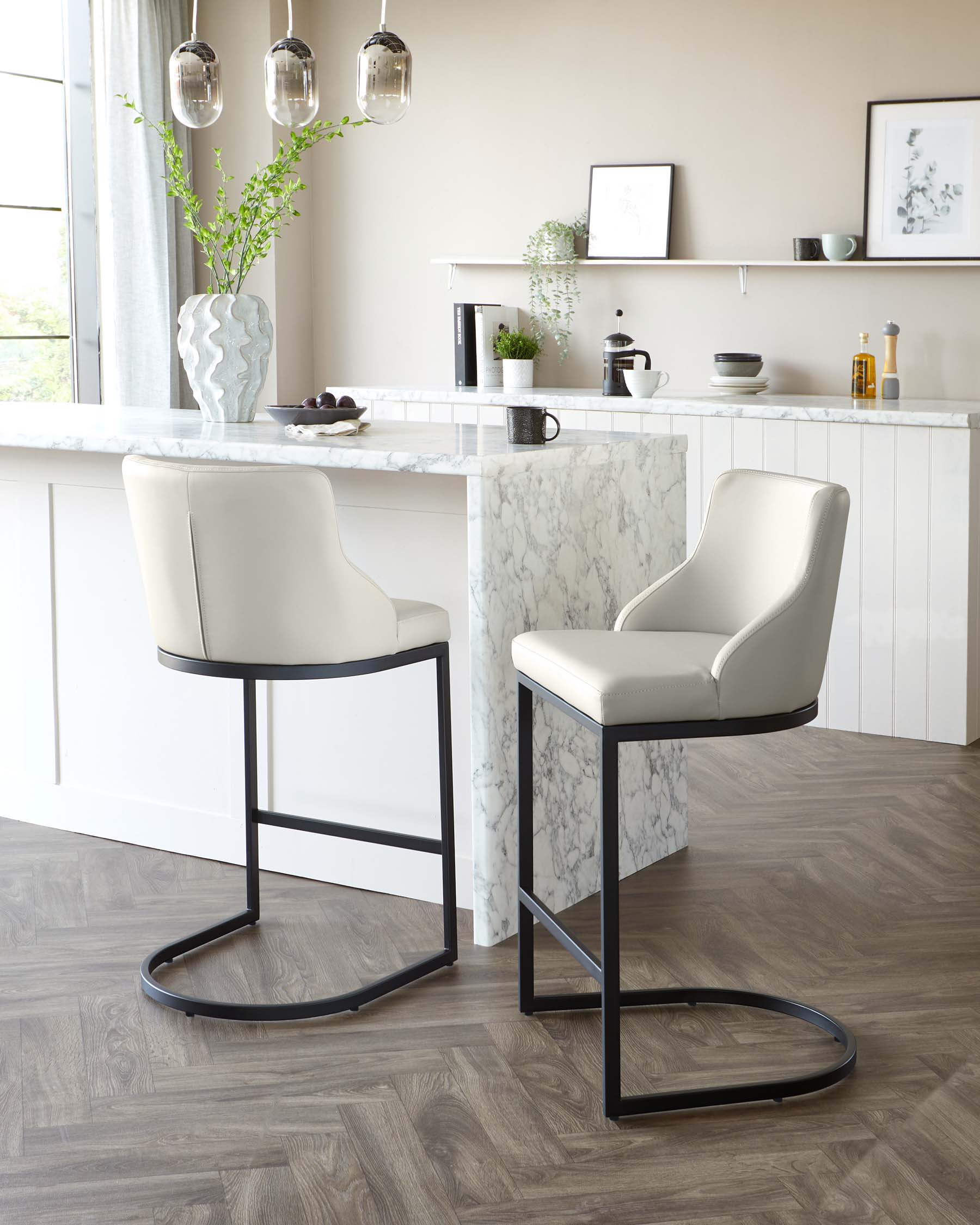 Two contemporary bar stools with sleek beige upholstery and slim black metal legs positioned at a modern kitchen island with marble countertop.