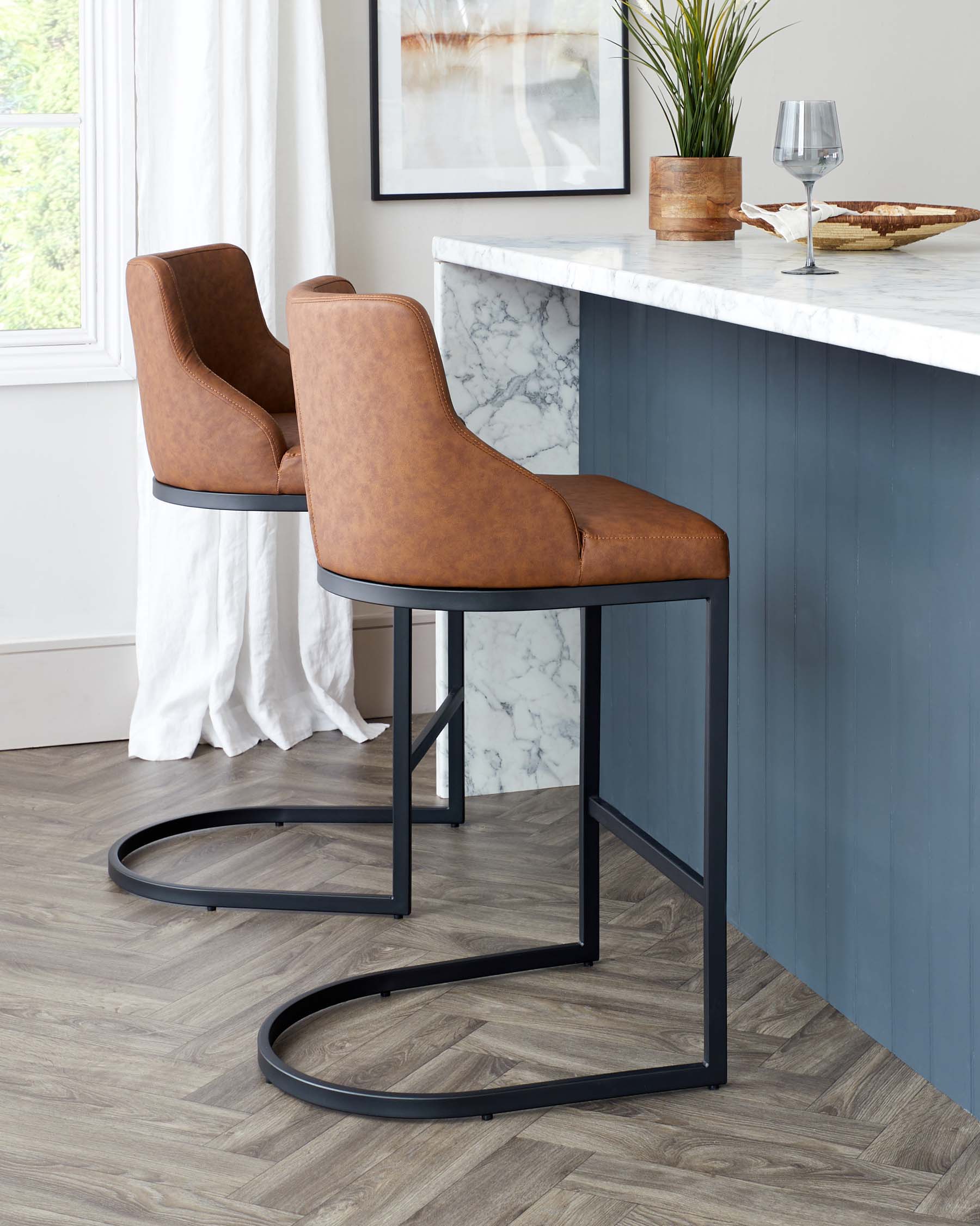 Two modern bar stools with sleek curved backs, upholstered in caramel-brown faux leather, featuring comfortable seat pads and supported by minimalist black metal frames with a circular footrest.