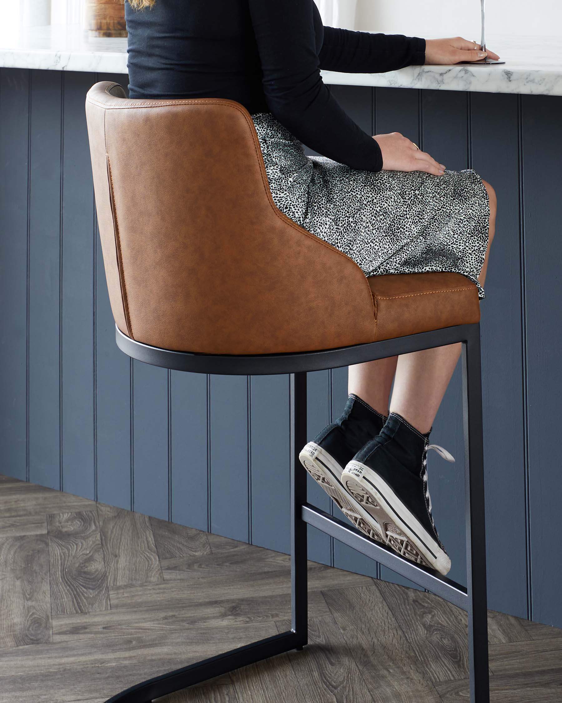 Modern bar stool with a curved backrest and tan faux leather upholstery, featuring a slender black metal frame with footrest.