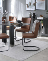 Modern dining room furniture featuring a rectangular table with a matte black finish and sleek, square legs. Four contemporary cantilever dining chairs with curved metal bases and cushioned seats upholstered in caramel brown faux leather. The ensemble is arranged on a light grey textured area rug.