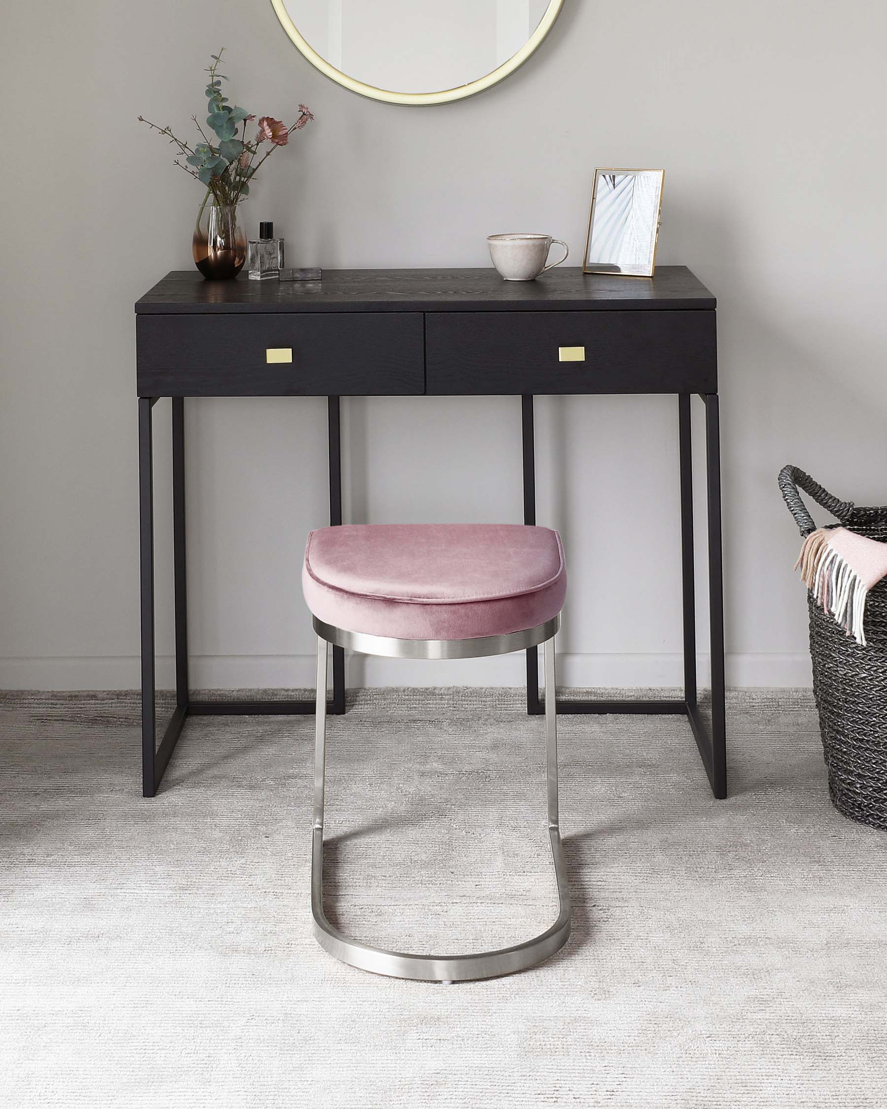 Contemporary black wooden console table with sleek brass handles, paired with a modern round-backed pink velvet stool featuring a metallic silver base. A round golden-rimmed mirror hangs above the table on a neutral wall.