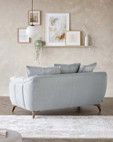 Elegant light grey fabric sofa with a curved backrest and rounded arms, featuring plush cushioning and sitting on tapered wooden legs, displayed in a tastefully decorated room with neutral tones.