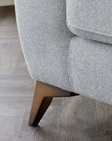 Close-up of a light grey textured fabric upholstered sofa with a focus on a tapered wooden leg with a natural finish.