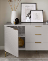 Modern grey sideboard with chevron textured door and sleek metallic handles, featuring three drawers and tapered gold legs.