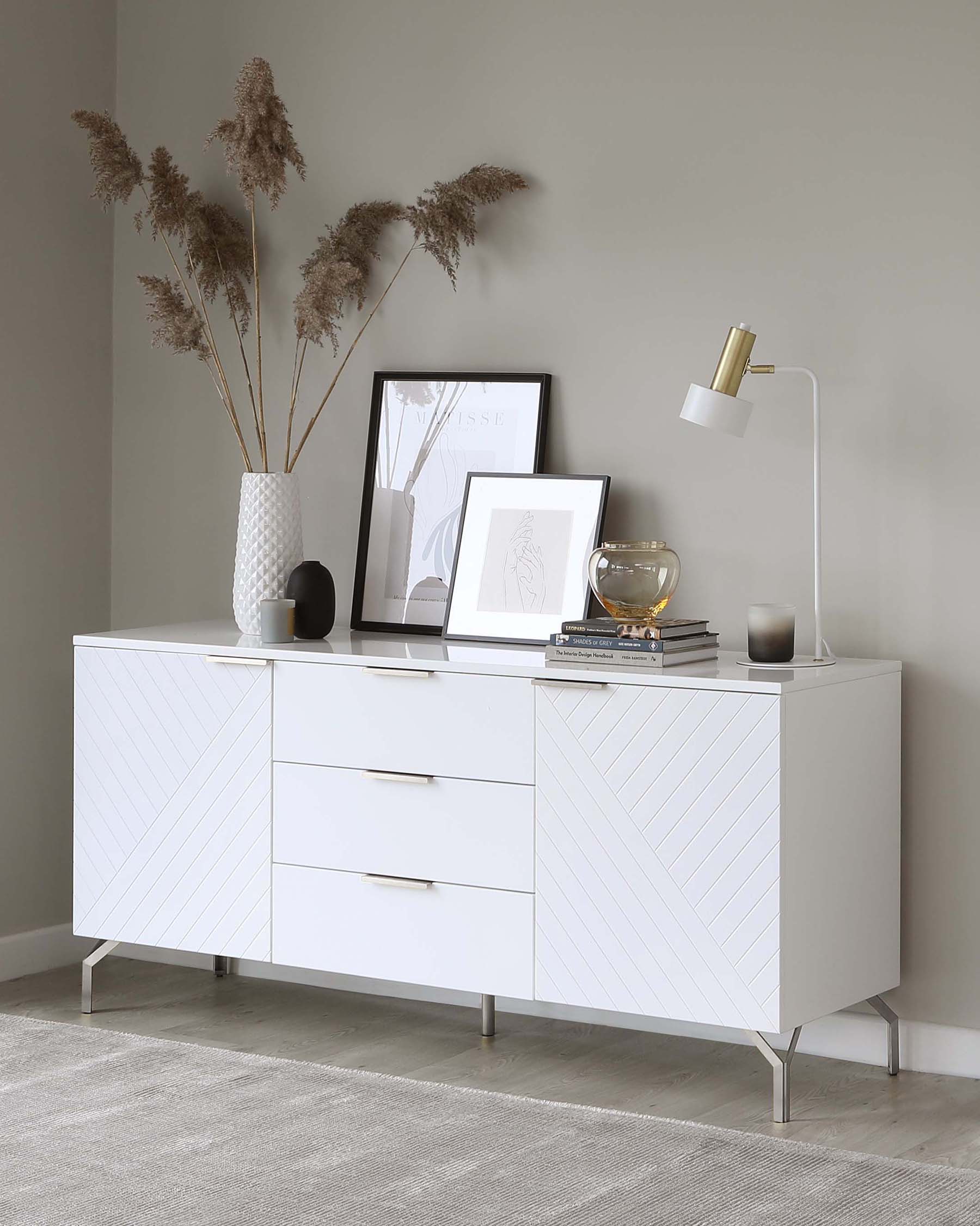 Modern white sideboard with geometric line detailing and metallic handles, elevated on sleek metal legs.