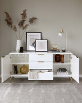 Modern white sideboard with multiple storage compartments, including shelving, drawers, and a cabinet, accented by brass handles, set against a neutral-toned wall.