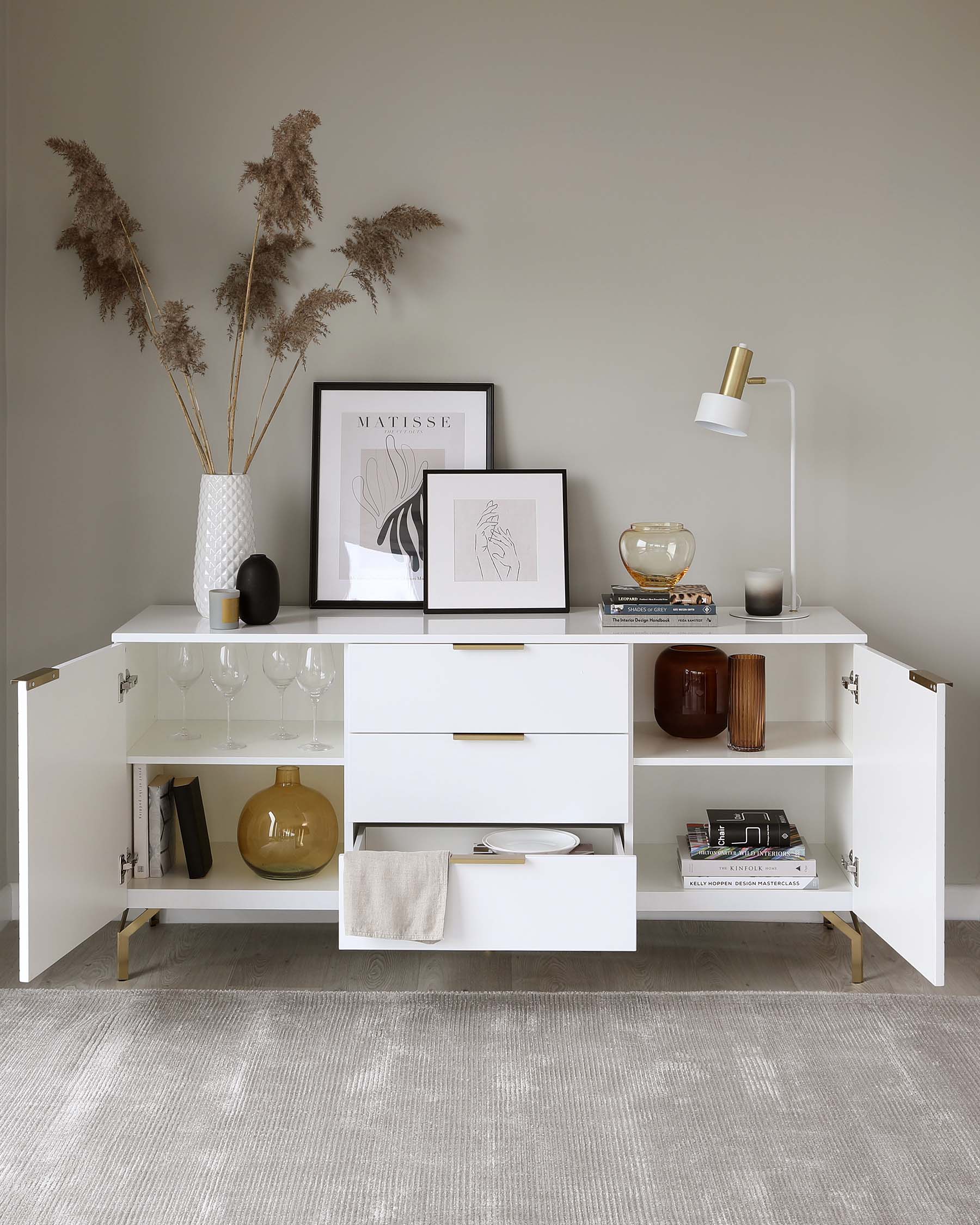 Modern white sideboard with multiple storage compartments, including shelving, drawers, and a cabinet, accented by brass handles, set against a neutral-toned wall.