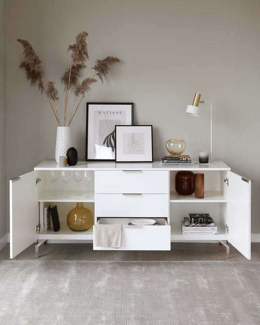 Modern white sideboard with multiple storage compartments, including shelves, drawers, and hinged cabinets, accentuated with minimalist metallic handles, on a light grey textured flooring.