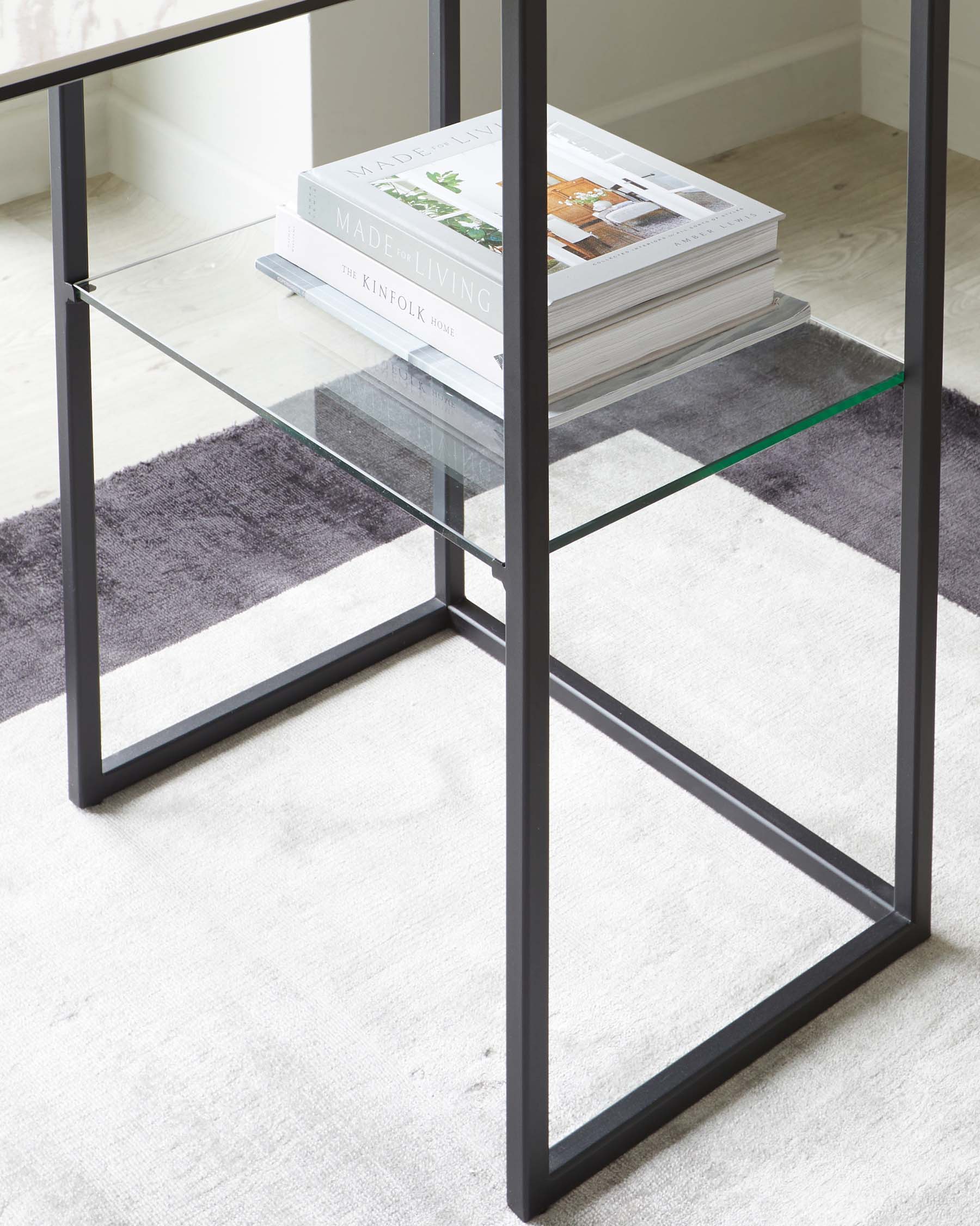 Modern minimalist glass-top side table with a sleek black metal frame, featuring an open lower shelf for additional storage or display.