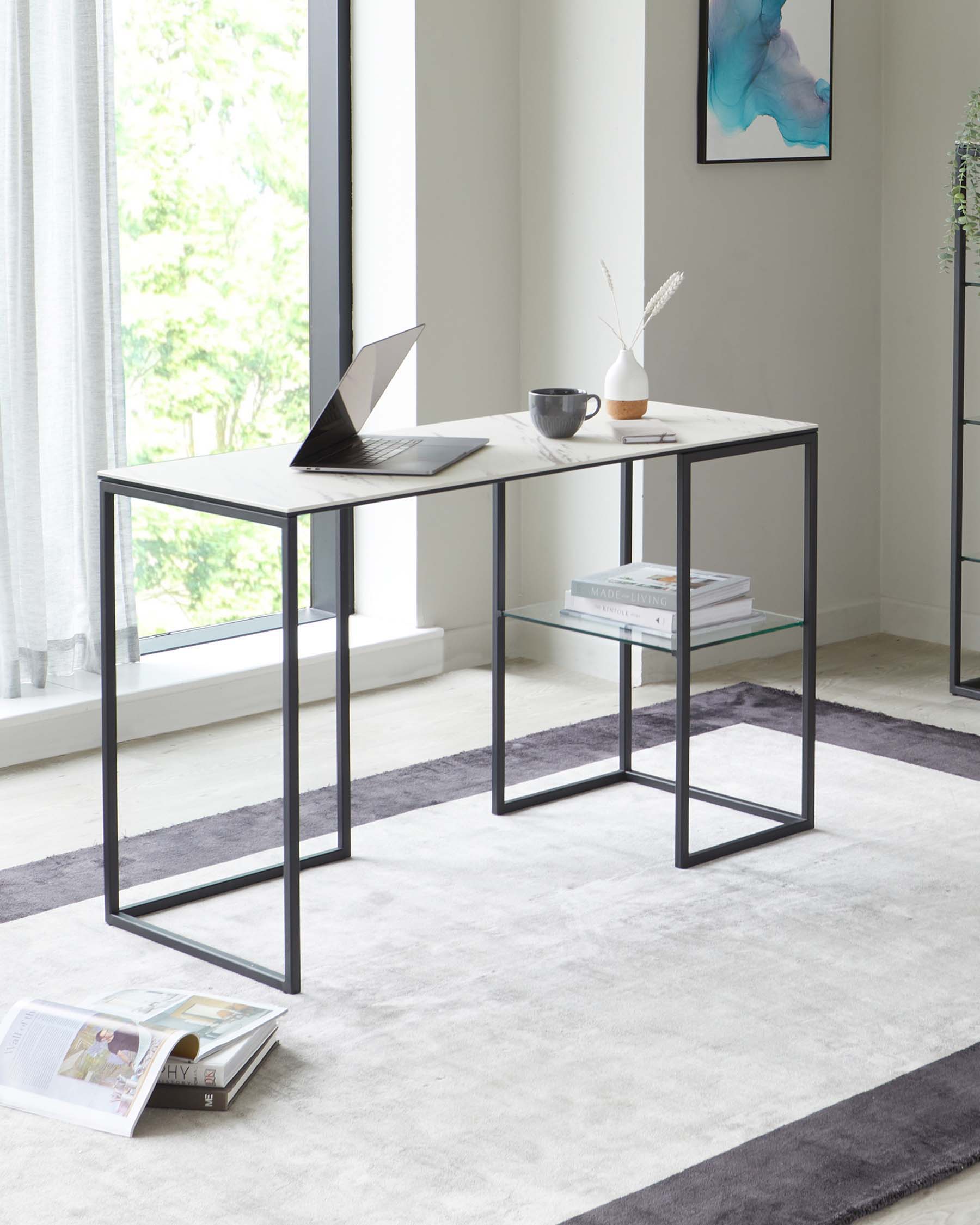 Modern minimalist two-piece desk set with a sleek black metal frame and white marble effect tabletop. The desks can be nested together or used separately, providing a versatile workspace solution. The larger desk is accessorized with a laptop, a coffee mug, and a small vase with two plumes, while the smaller desk displays a stack of books. They rest on a soft, two-tone grey area rug in a well-lit room with a view of greenery outside the window.