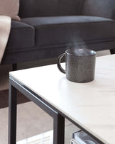 Modern minimalist coffee table with a white marble top and black metal legs, accompanied by a sleek dark upholstered sofa in the background.