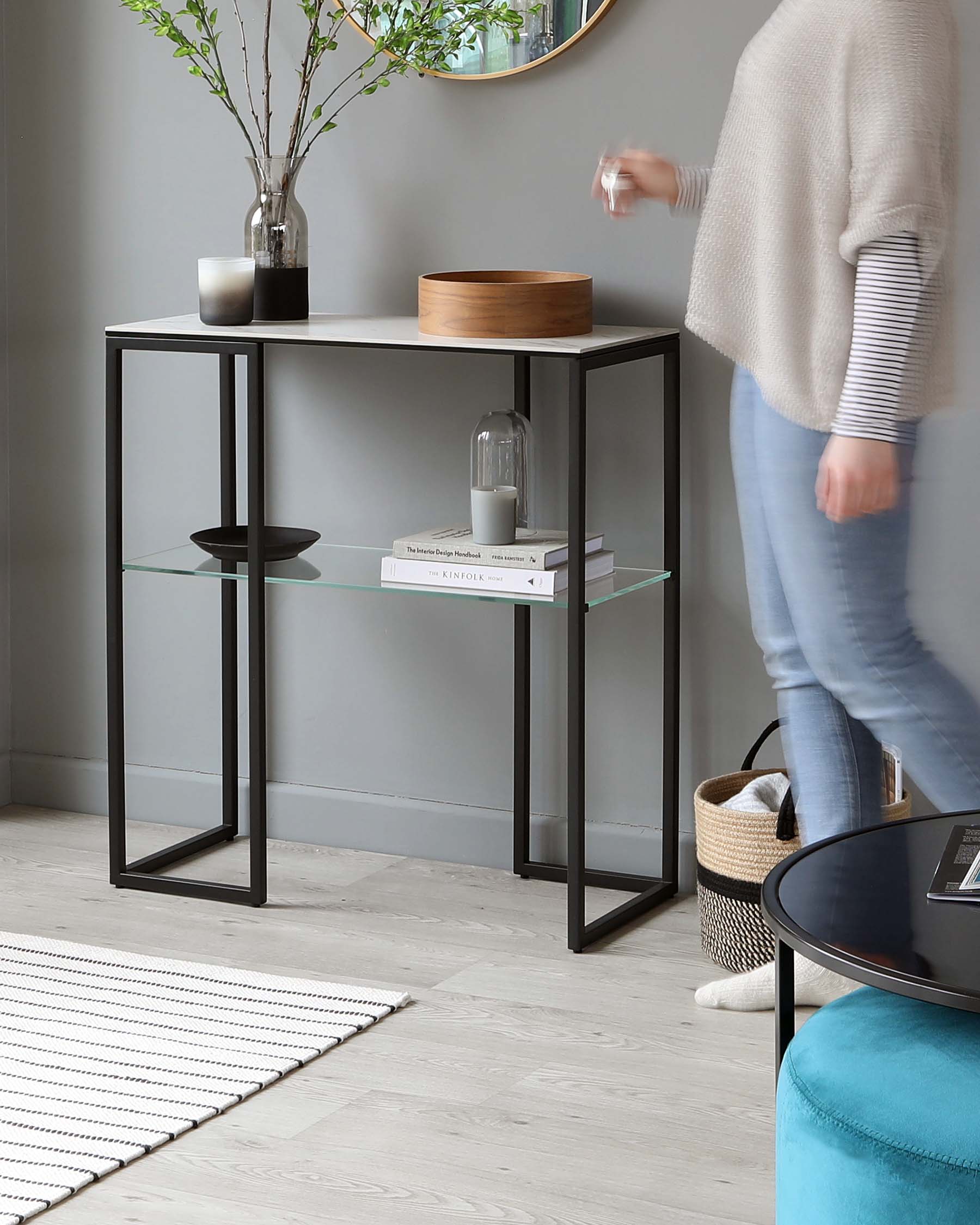 Modern rectangular console table with a matte black metal frame and two tiers of shelving, one glass and one solid, showcasing decorative items and books.