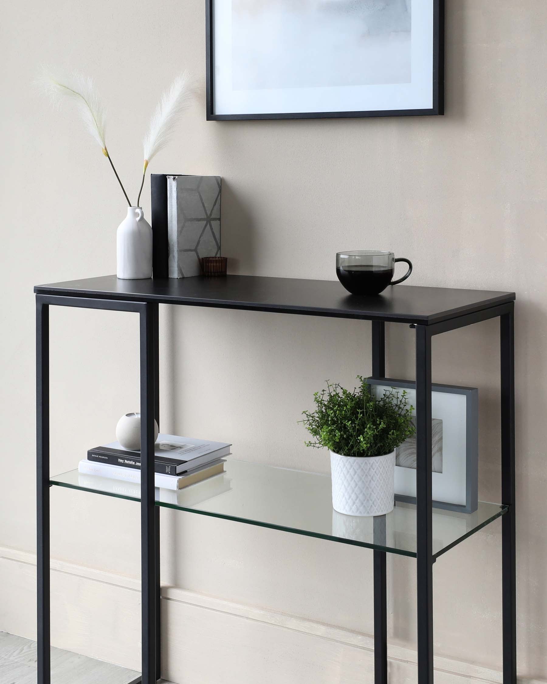 Modern black metal frame console table with three tiers, featuring two glass shelves and one solid black shelf, adorned with decorative items such as vases, books, and a plant.