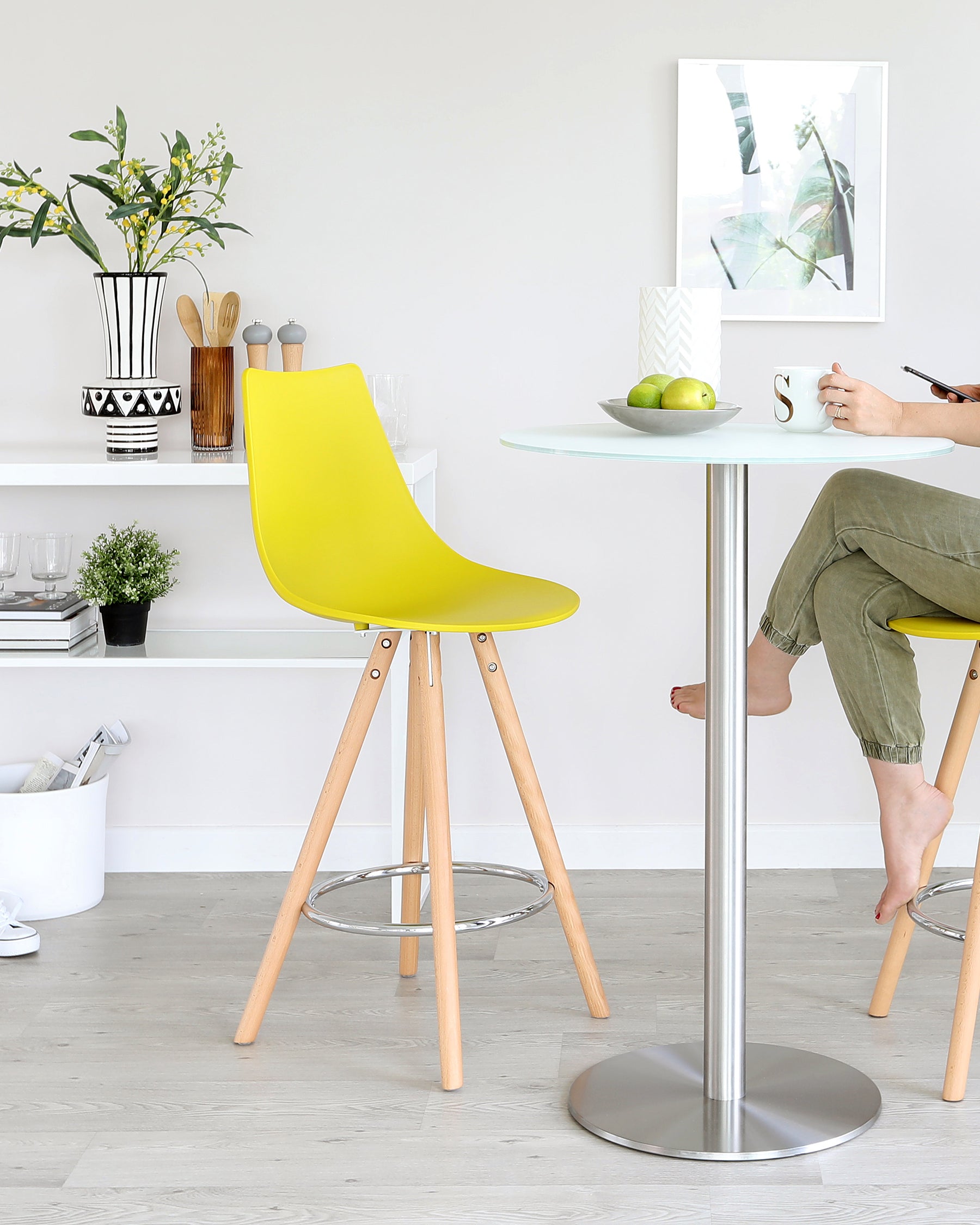 Modern bright yellow chair with a sleek, curved design and wooden legs, paired with a round white high-top table with a metallic base.