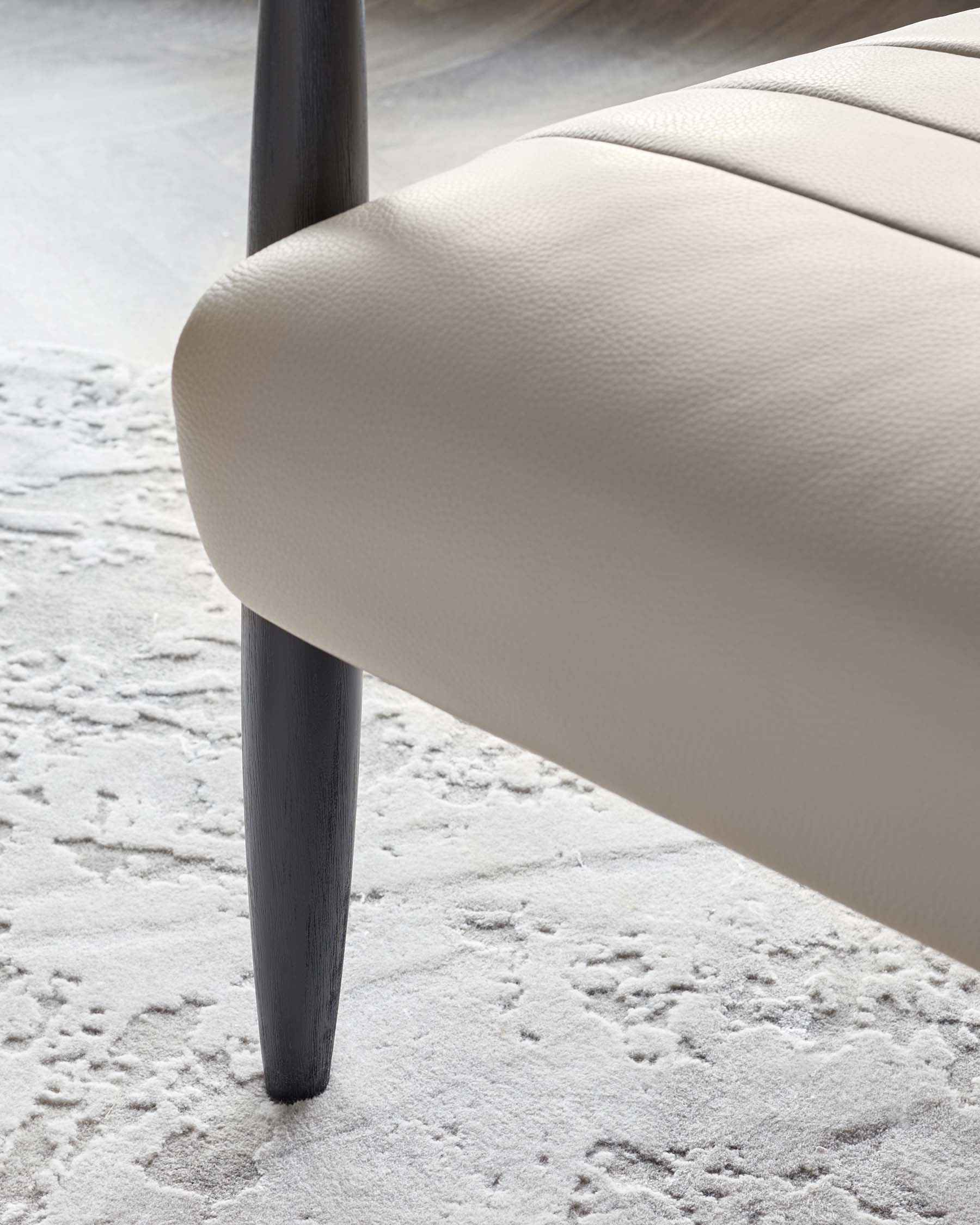 Close-up view of a beige upholstered chair with diamond tufting, featuring sleek black wooden legs, positioned on a textured white rug.