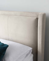 Elegant beige upholstered headboard with vertical stitching and curved corners, partially shown with white bed linen and a teal accent pillow.