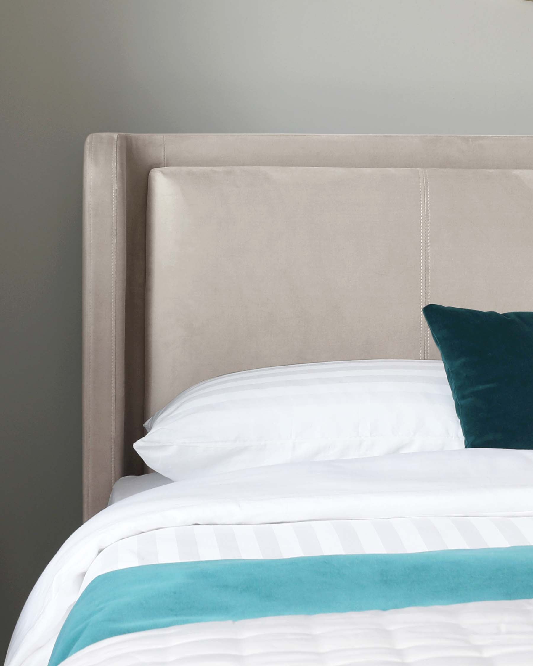 Elegant neutral-toned upholstered headboard featuring a subtle wingback design and decorative nail head trim, accompanied by crisp white bedding with a bold turquoise stripe and a plush velvet teal throw pillow.