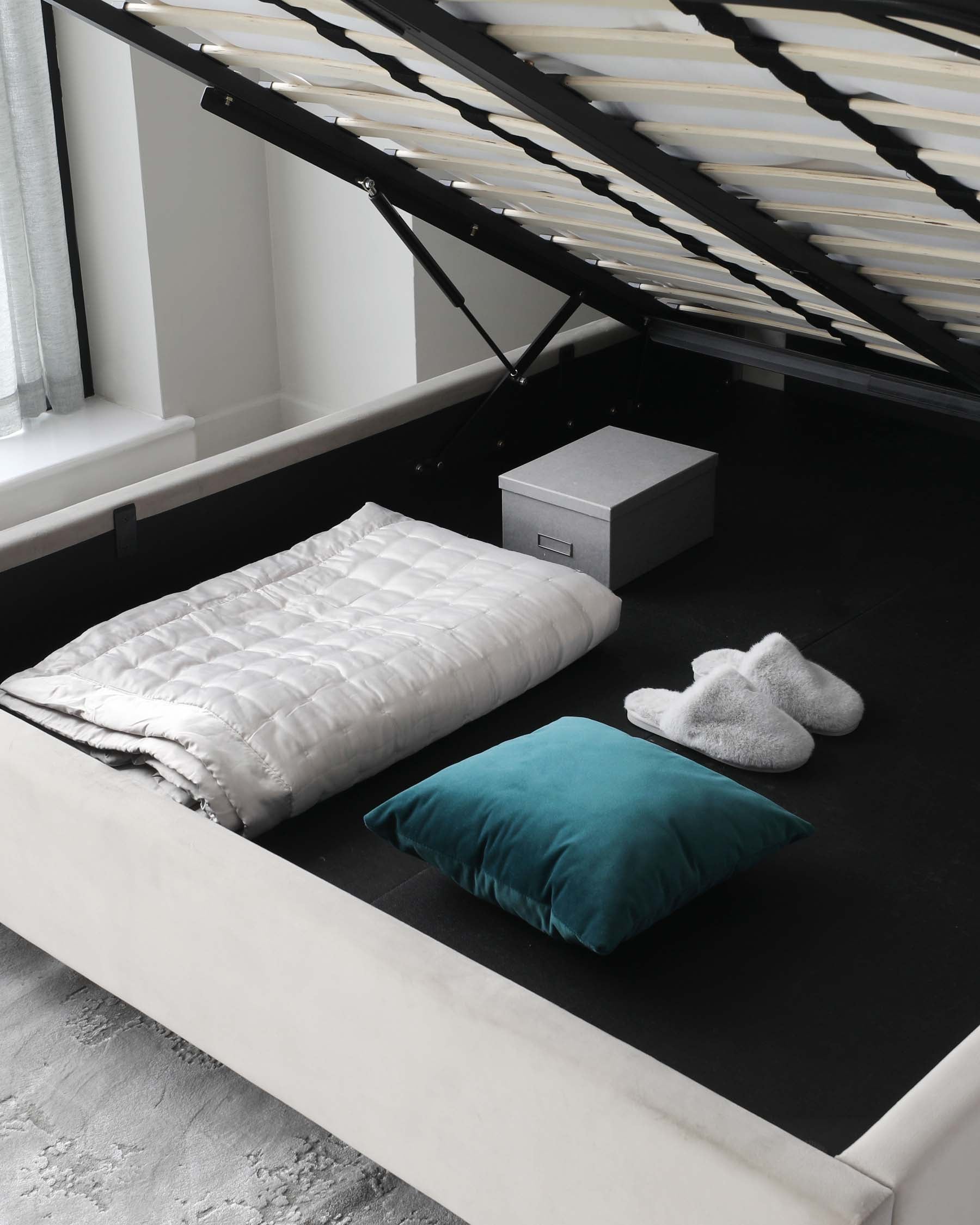 Modern minimalist style platform bed with a white frame and integrated headboard, complemented by a dark mattress. The bed features a gas-lift mechanism revealing under-bed storage. Accessories include a quilted white comforter, a teal throw pillow, and a pair of white fuzzy slippers on a black textured rug.