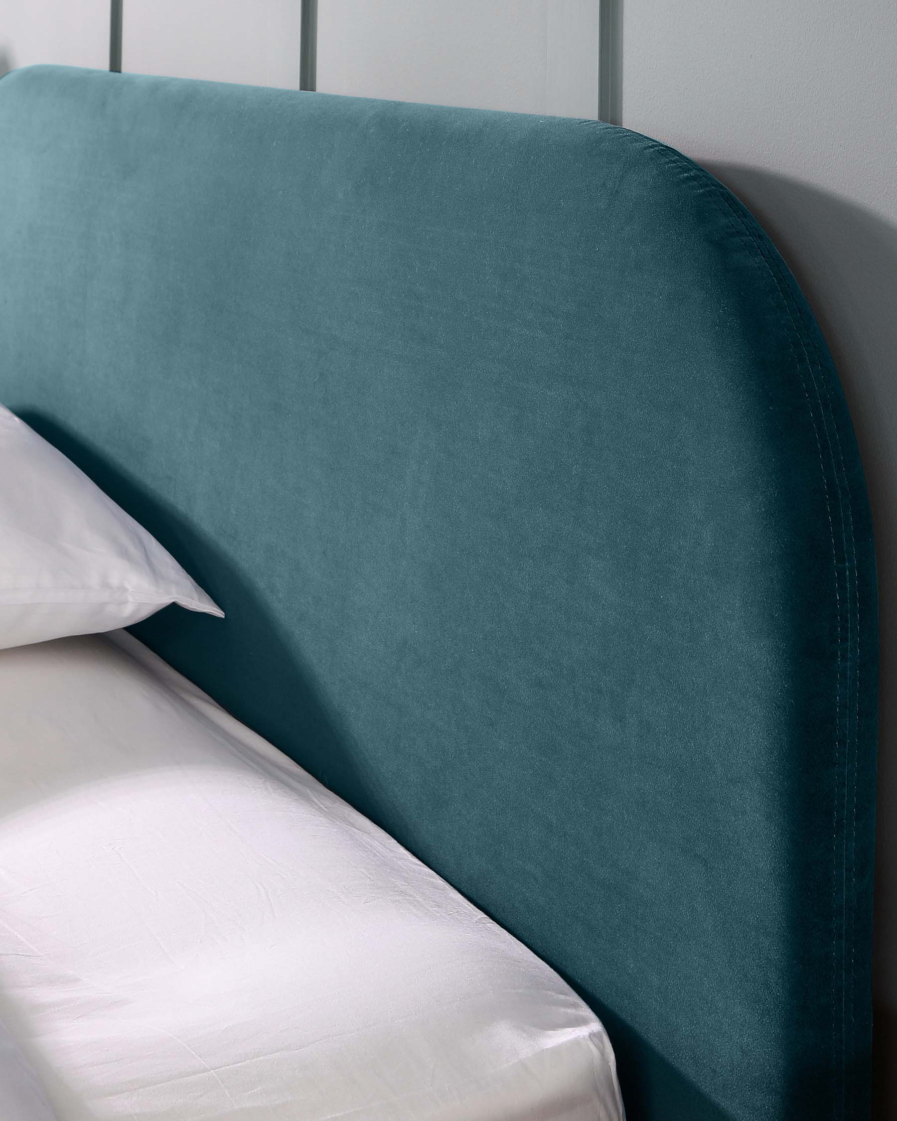 Elegant teal upholstered headboard with a curved top and piped edges, against a white bedsheet and pillow.