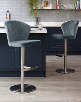 Two contemporary teal velvet bar stools with channel tufting on the backrest, swivel seats, integrated footrests, and adjustable height on a sleek brushed metal pedestal base, set against a modern kitchen counter.