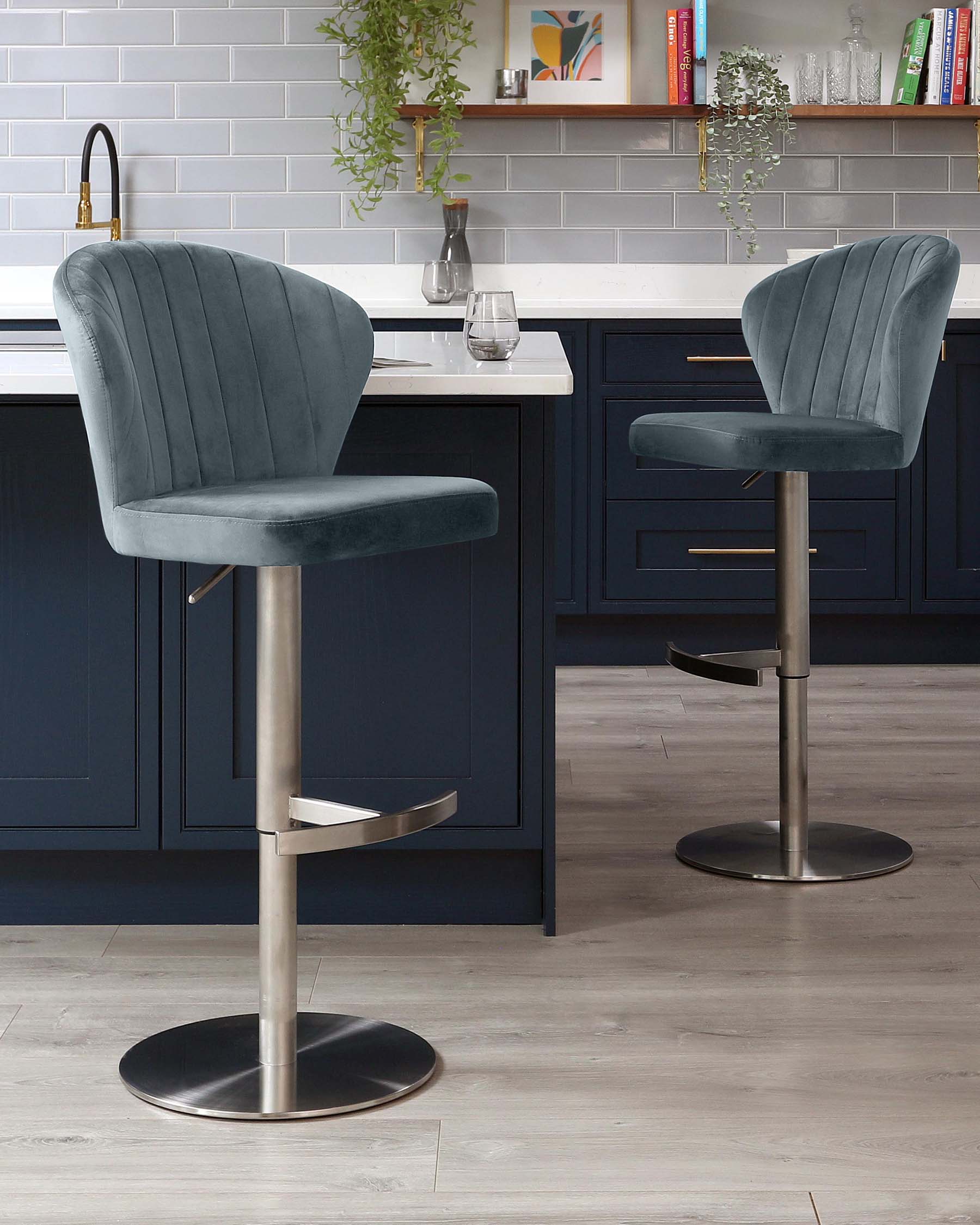 Two contemporary teal velvet bar stools with channel tufting on the backrest, swivel seats, integrated footrests, and adjustable height on a sleek brushed metal pedestal base, set against a modern kitchen counter.