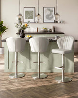 Modern kitchen interior featuring three luxurious white leather bar stools with channel tufting, adjustable height, and chrome pedestal bases, complementing a pastel green kitchen island with a dark countertop.