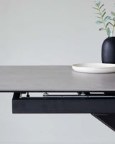 Minimalist modern table with a dark grey matte finish tabletop and slim, black metal frame, highlighted with a decorative ceramic plate and a vase with eucalyptus branches on top.