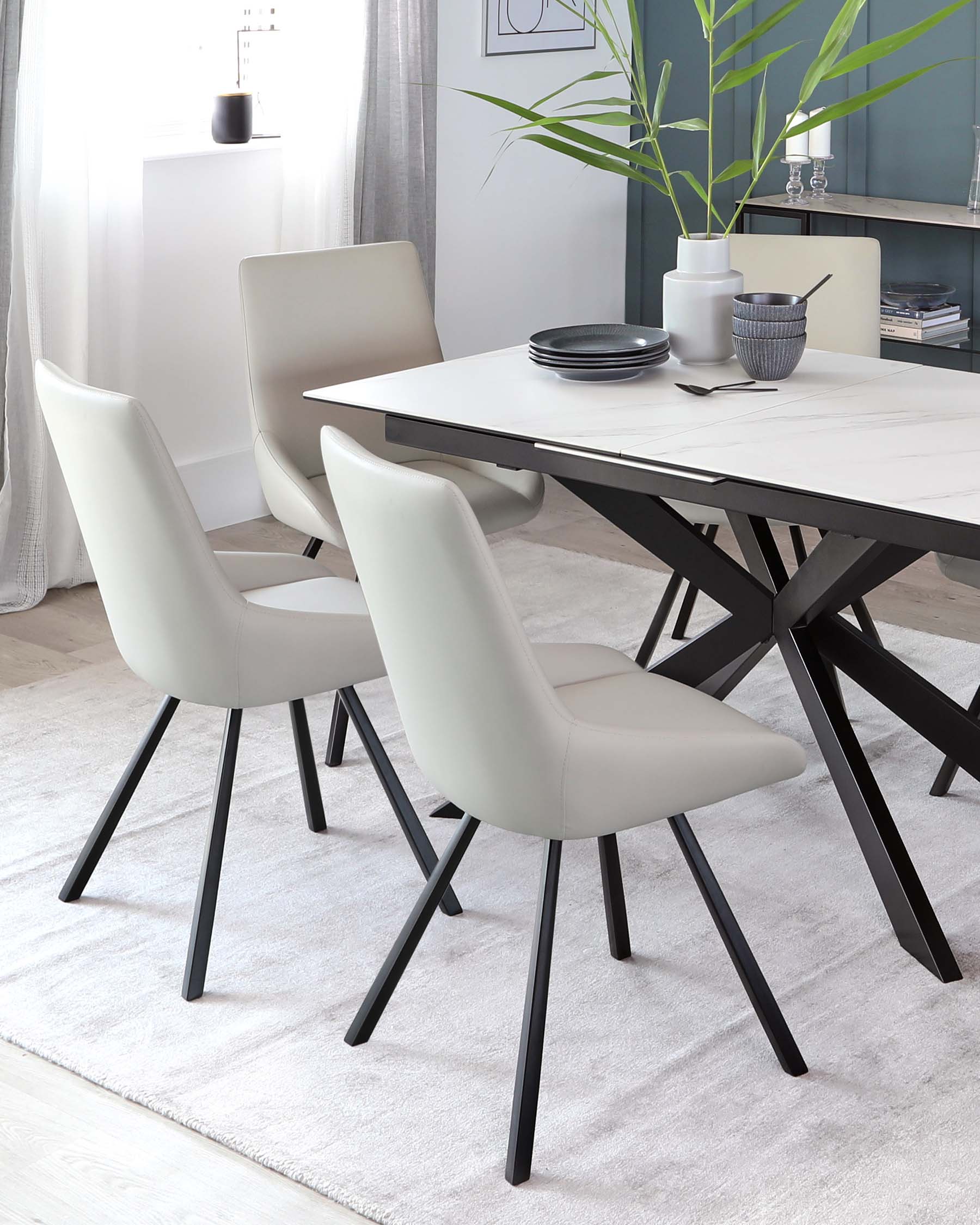 Modern dining room setting featuring a white marble top table with a unique geometric black base and three light beige upholstered chairs with a minimalist black metal leg design.