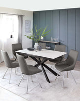 Contemporary dining set with a white rectangular table featuring a unique black crisscross base design and six grey upholstered chairs with sleek metal legs, all arranged on a soft grey area rug.