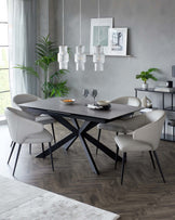 Modern dining room set featuring a rectangular table with a matte black top and a striking geometric black metal base. Accompanied by six sleek, upholstered chairs in a light grey colour with slim black metal legs. A minimalist black metal shelf with various decorative items and plants is in the background. The scene is complemented by elegant pendant lights and framed artwork adding sophistication to the contemporary design.