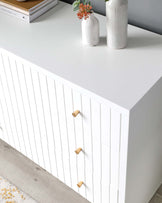 Modern white dresser with clean lines, featuring 3D linear texture and natural wooden knobs, accompanied by minimalistic decorative vases on top.