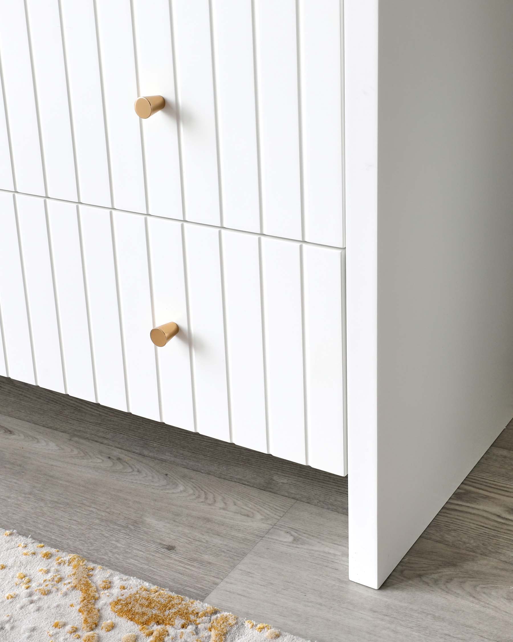 Minimalist white chest of drawers with vertical ridges and wooden knobs against a grey wooden floor and partial view of a textured rug with yellow accents.