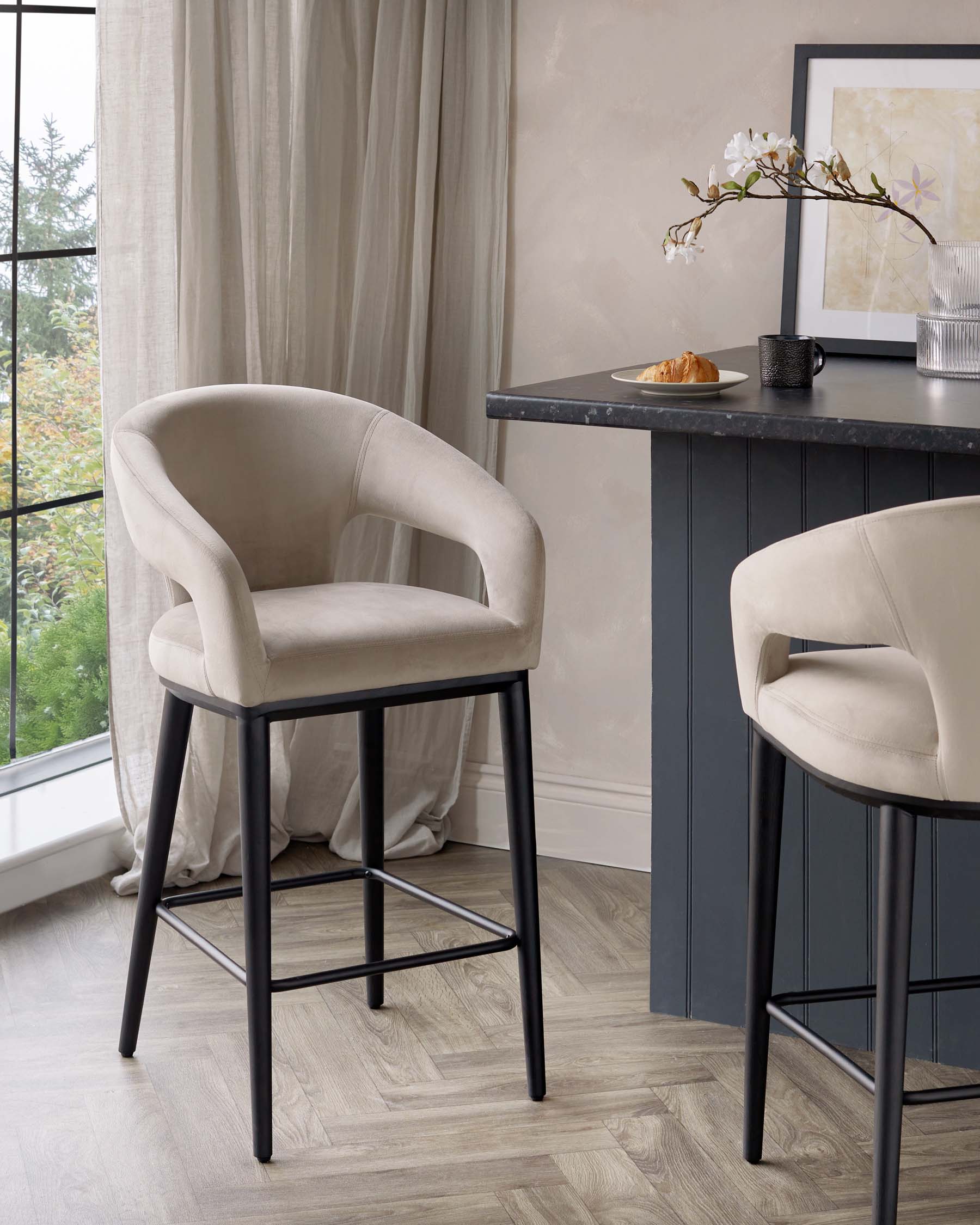 Elegant contemporary bar stool with a beige upholstered curved seat and backrest on a sleek black metal frame with footrests, paired with a sophisticated black bar table with a matte finish, in a room with soft natural light.