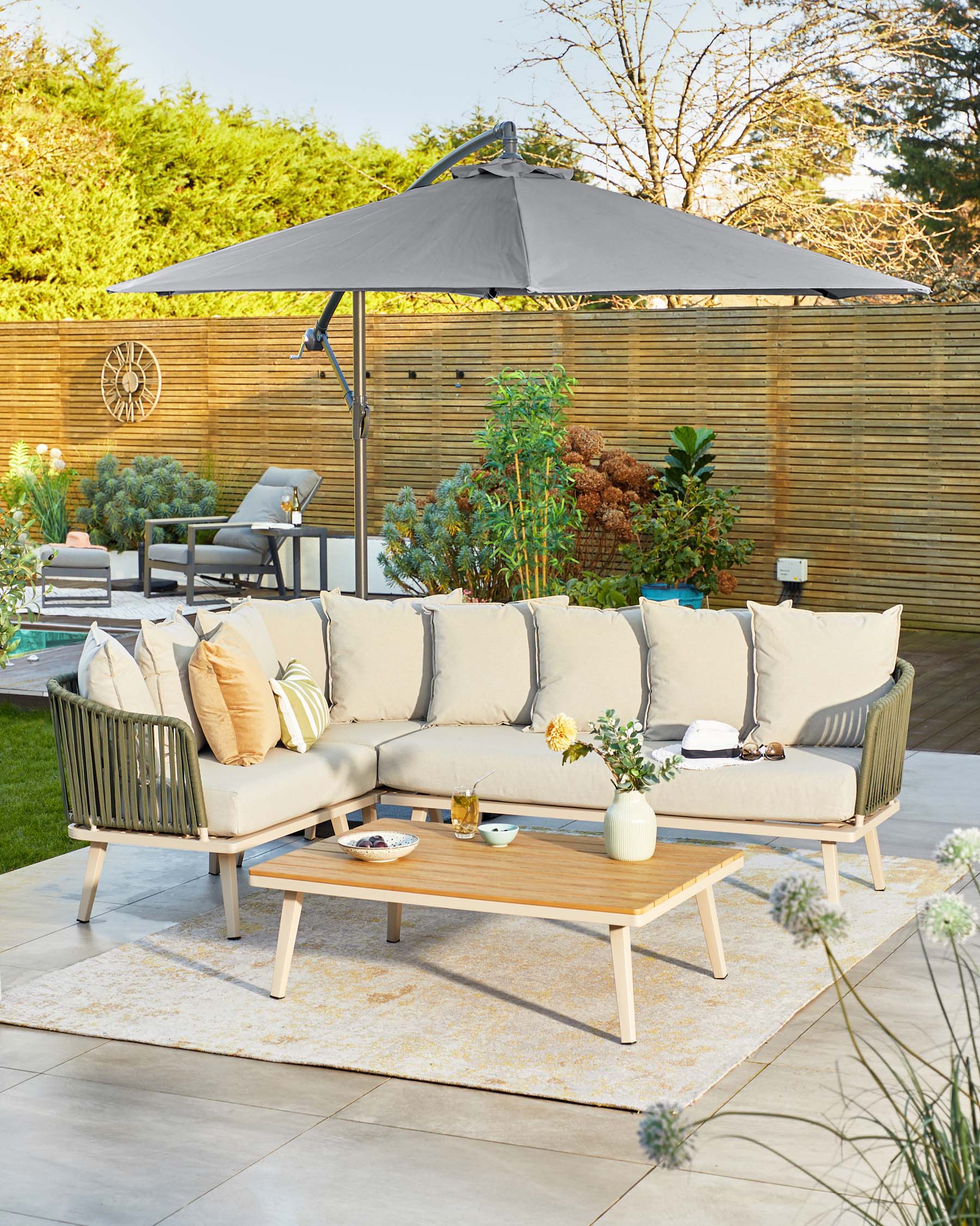 A beige sectional sofa with cushions, a wooden coffee table, and a stylish umbrella, set on a decorative outdoor rug.