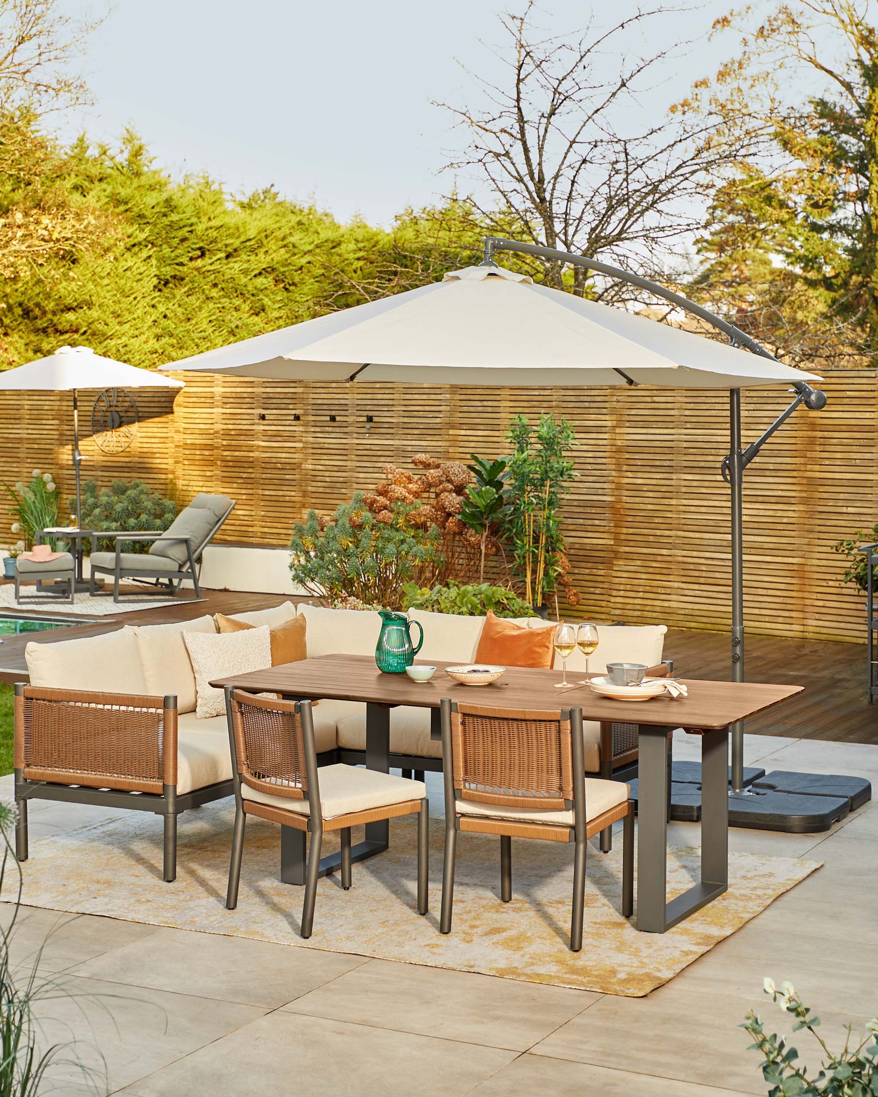 Outdoor dining set featuring a rectangular table, cushioned corner sofa, four woven chairs, and a large umbrella for shade.