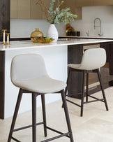 Modern kitchen bar stools with a minimalist design, featuring light grey upholstered seats and matte black metal legs.