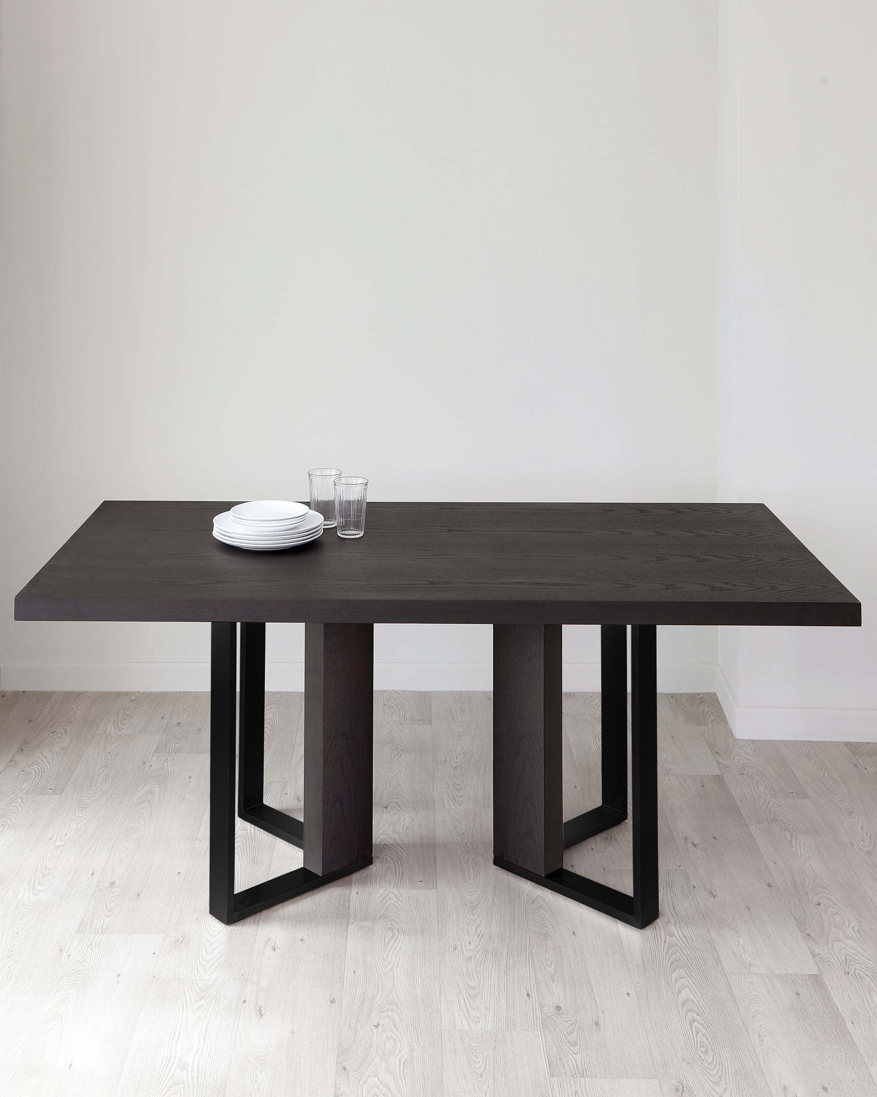 Modern dark wood dining table with a minimalist design featuring straight lines and rectangular legs, displayed in a room with light hardwood flooring and white walls. Table is set with a simple arrangement of white plates and clear glasses.