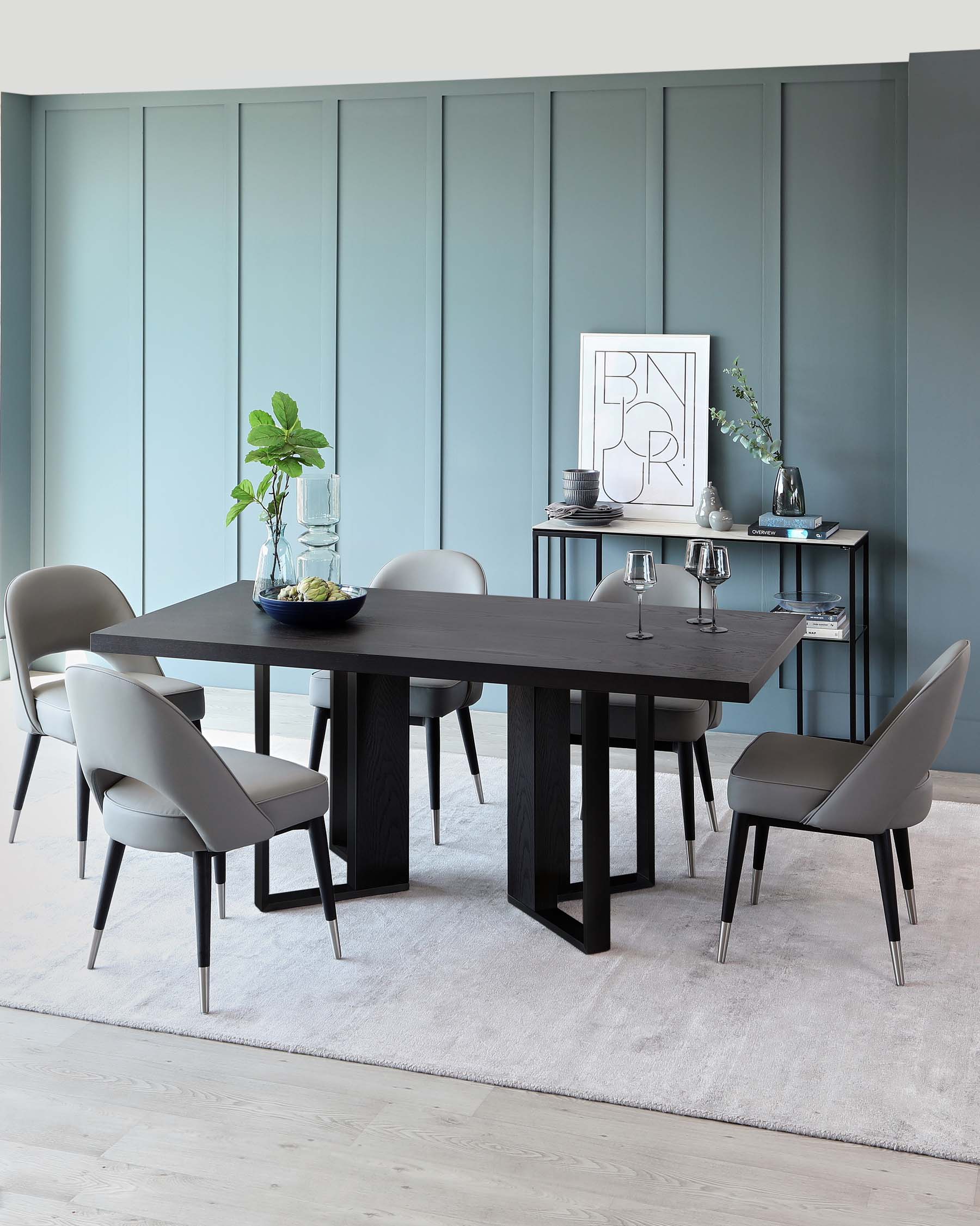 Modern dining room furniture set featuring a rectangular black wooden table with thick, vertical slab legs, paired with four sleek grey upholstered chairs with black wooden frames and angled, tapered metal legs. A minimalist two-tiered black shelving unit stands to the right holding decorative items. The set is accentuated by a soft white area rug on light wooden flooring.