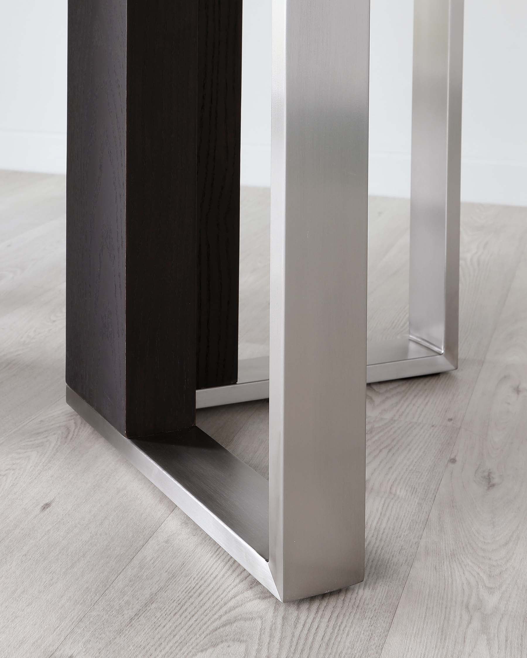 Close-up view of a modern furniture leg, featuring a dark wooden column attached to a polished silver metal frame, displayed on a light wooden flooring.