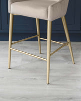 Elegant modern bar stool with a cushioned seat upholstered in light grey fabric and a sturdy metallic gold base with geometric legs and footrest.