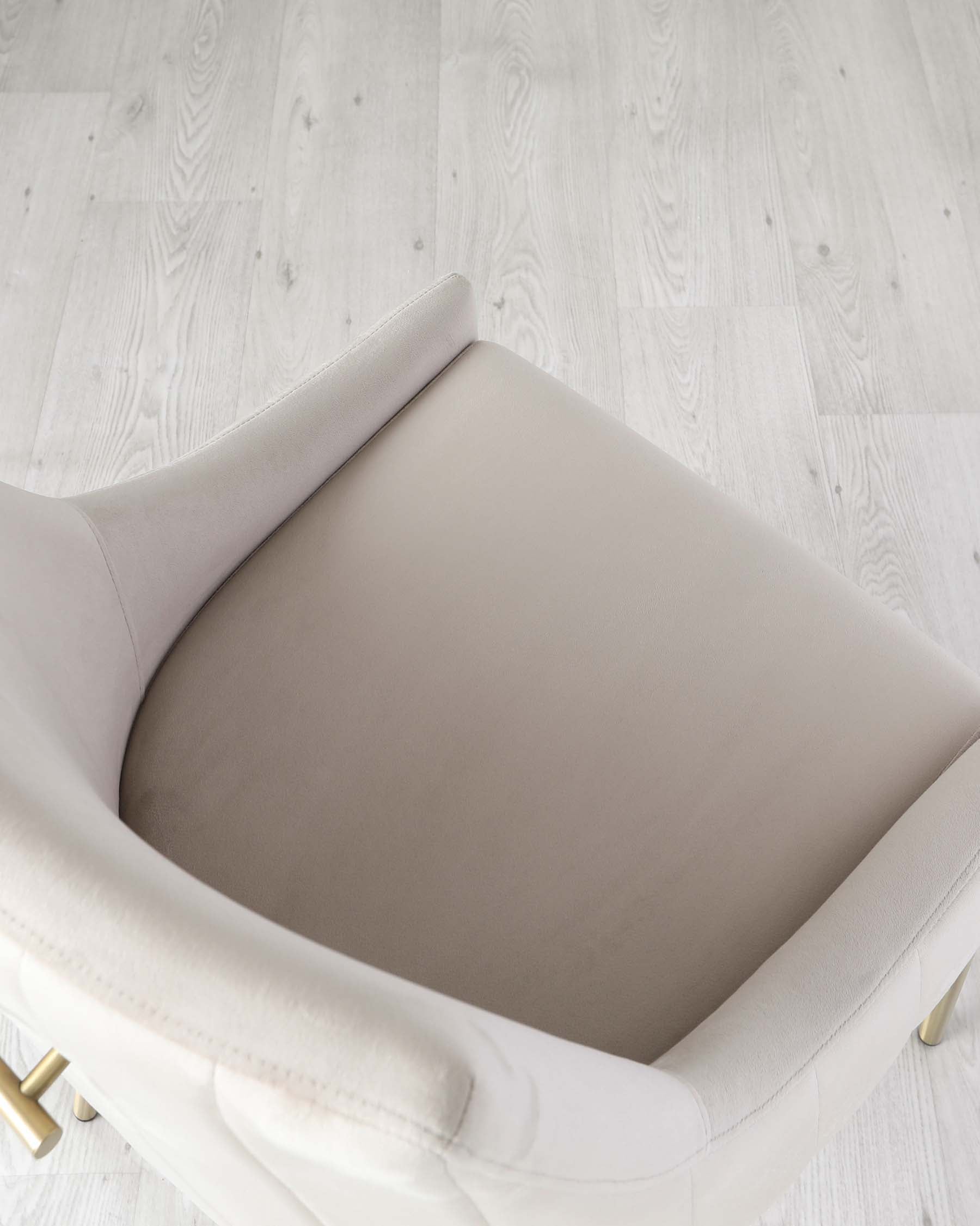 A close-up view of a modern, off-white armchair with elegant lines and brass legs on a light wooden floor.