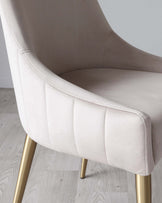 Elegant modern accent chair with cream upholstery and gold-finished metal legs. Features include a curved backrest, deep cushioned seat, and horizontal stitching on the outer side.