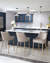 Elegant modern kitchen with three luxurious upholstered bar stools featuring high backs and gold-finished metal legs. The seating is complemented by a sleek white countertop bar.