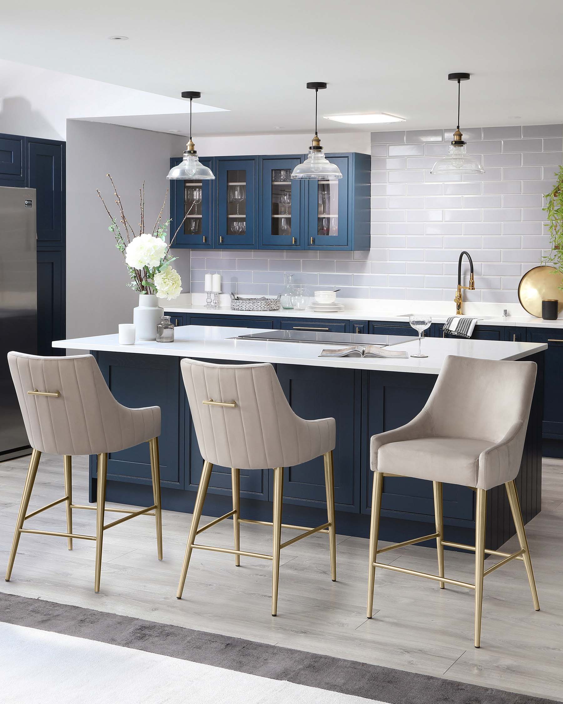 Elegant modern kitchen with three luxurious upholstered bar stools featuring high backs and gold-finished metal legs. The seating is complemented by a sleek white countertop bar.