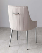 Modern light beige upholstered chair with vertical stitching detail on the backrest and sleek silver metal legs positioned on a pale wooden floor against a soft grey wall.