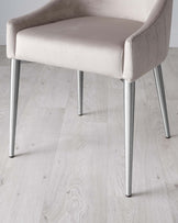 Modern elegant chair with a curved backrest and plush beige upholstery on a solid seat, featuring sleek metal legs in a silver finish. The chair is positioned on a light wooden floor, highlighting its contemporary design suitable for a minimalist or chic interior.