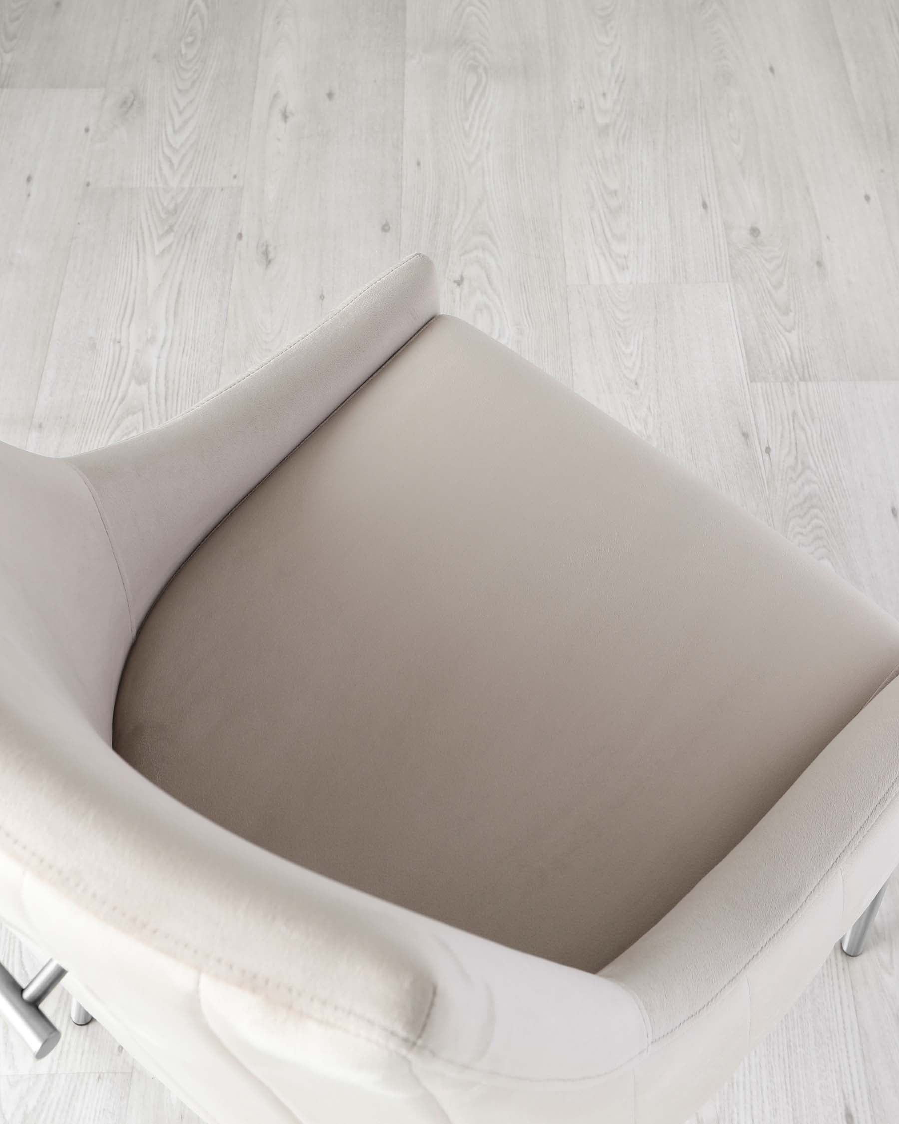 Modern minimalist armchair with a light beige upholstered seat and curved backrest, featuring clean lines and metal legs, displayed on a light wooden floor.