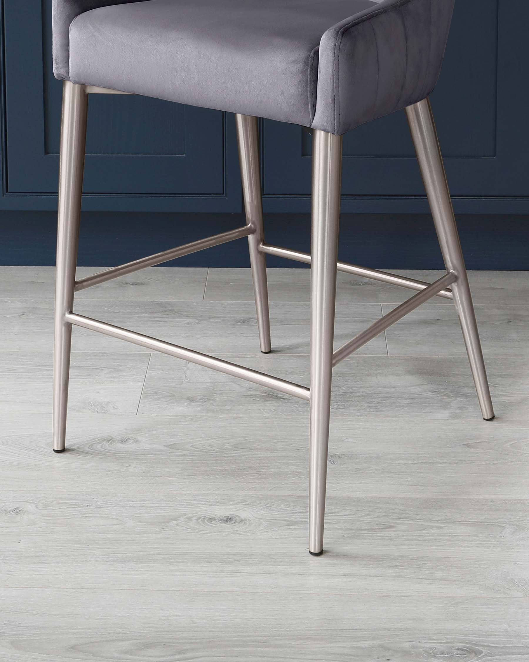 Modern bar stool with grey upholstery and metallic finished legs set against a blue wall and light wooden floor.